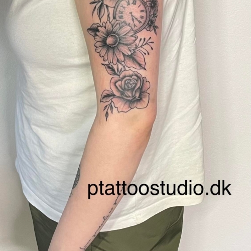 Tatovering af blomster og ur på overarmen lavet af P Tattoo Studio i Ikast